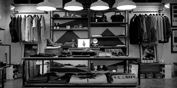 Wall of a retail store, lined with clothes on rails and shelves, black and white thumbnail